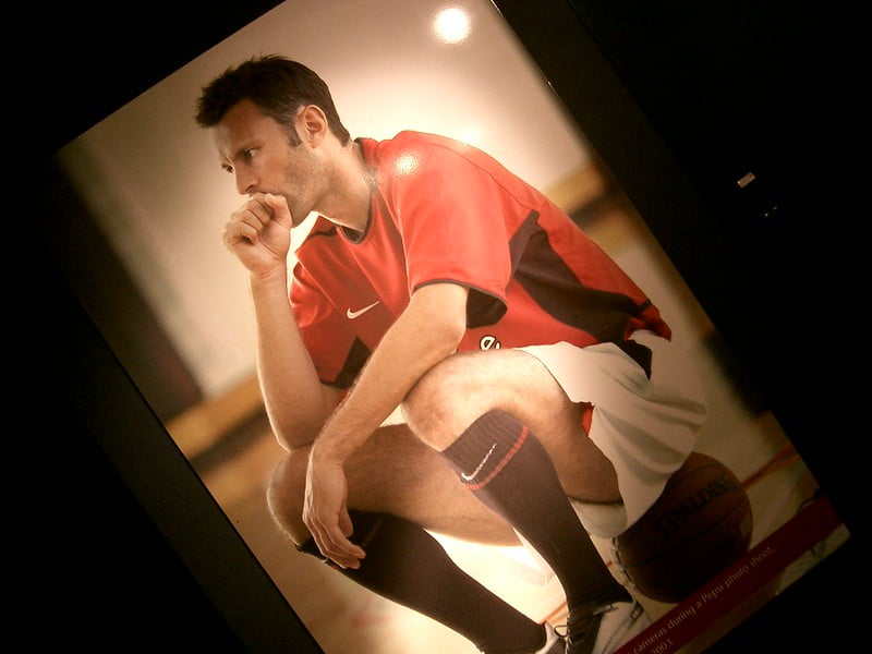 A photo of a man is sports gear sat on a ball, looking worried